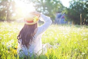 langhaarige Frau sitzt mit Strohhut auf Sommerwiese in der Sonne