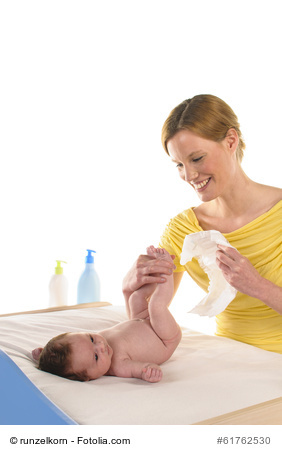 Eine lächelnde junge Frau windelt ihr Baby.